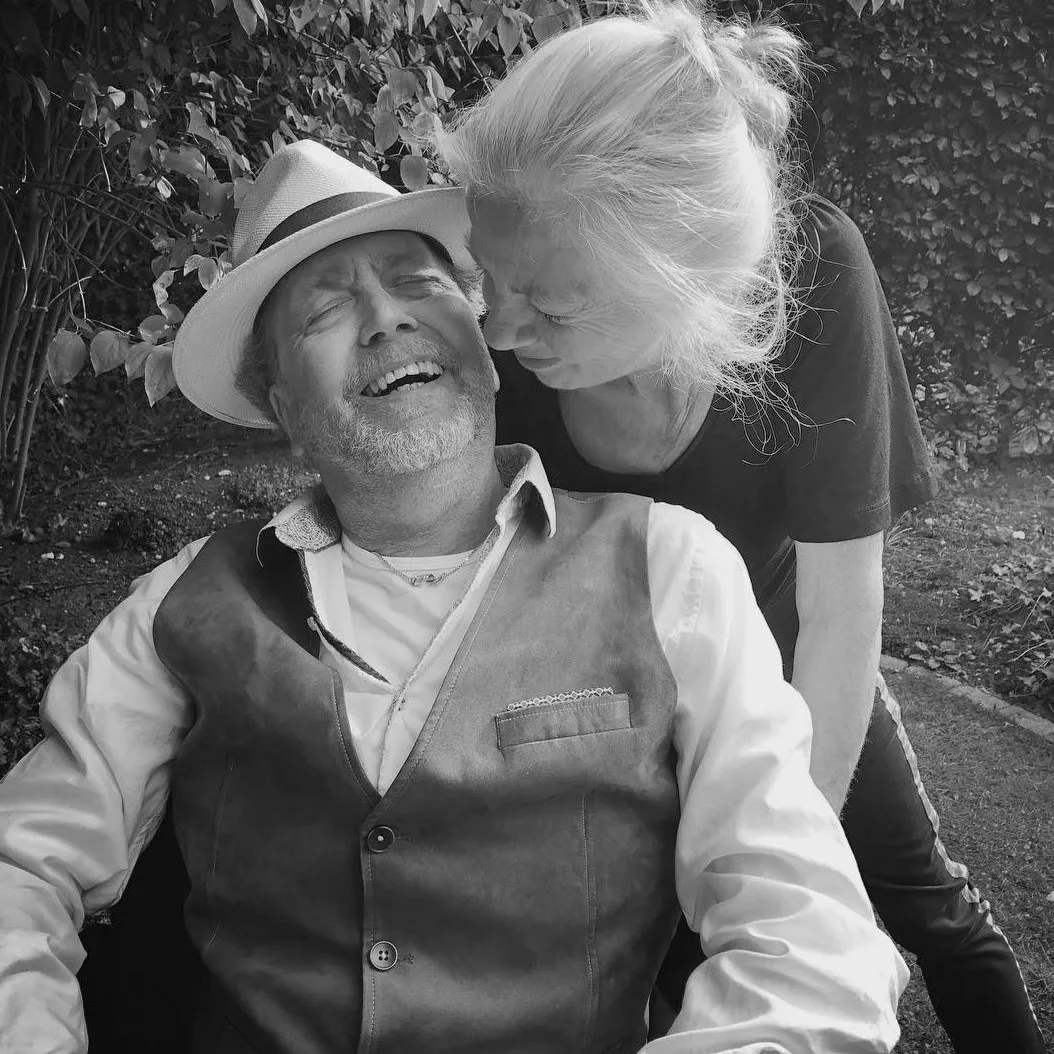Pieter lacht met zijn ogen dicht; zijn vrouw buigt zich over hem heen, haar gezicht tegen het zijne